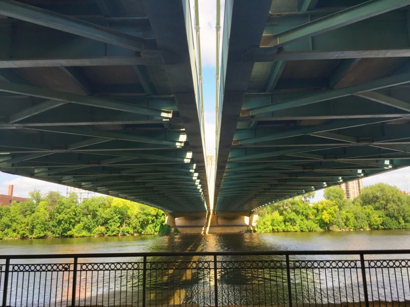 Looking up at the green steel truss and deck girders beneath a Mississippi River bridge